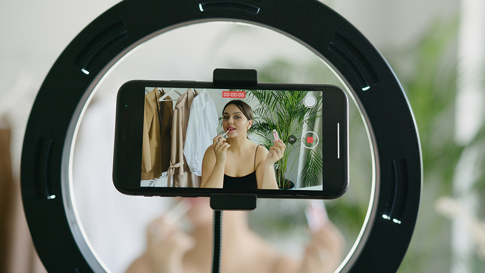 Vrouw maakt zichzelf op, neemt het proces op met haar smartphone en een ringlicht gericht op haar. Een inkijk in beauty-vlogging.