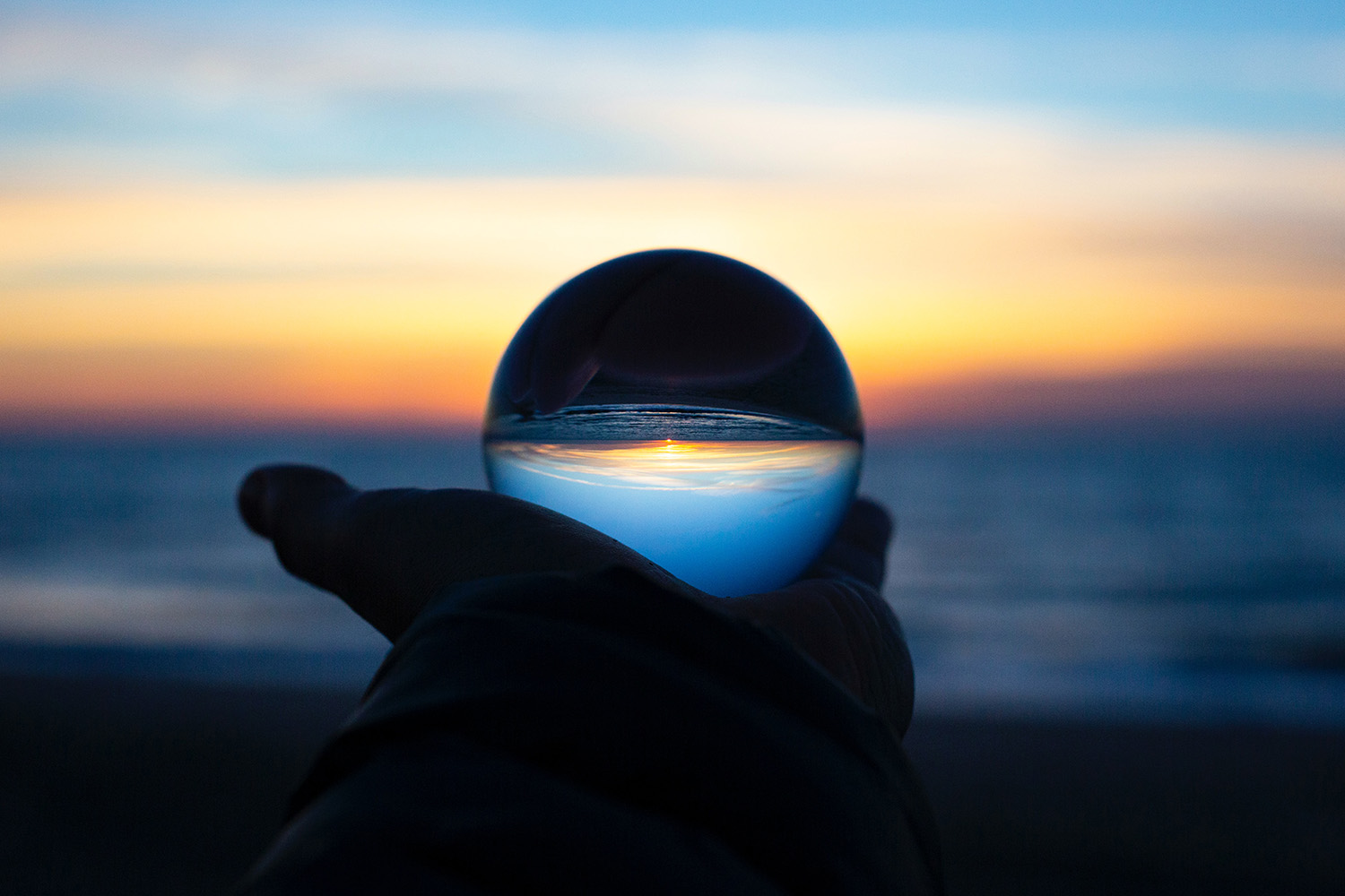 Hand die een glazen bol vasthoudt met een horizon en de zee op de achtergrond, symboliseert te kunnen voorspellen wat de toekomst te bieden heeft.